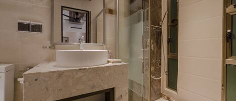 A bathroom with a marble sink, a glass shower enclosure, and a built-in shelf with toiletries.