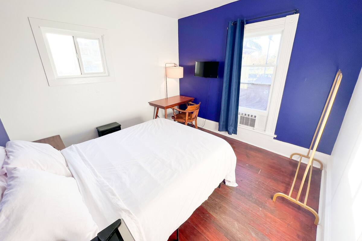 Ein Hotelzimmer mit einem Bett, einem Schreibtisch, einem Sessel, einem Fernseher und einem Fenster mit Vorhängen.