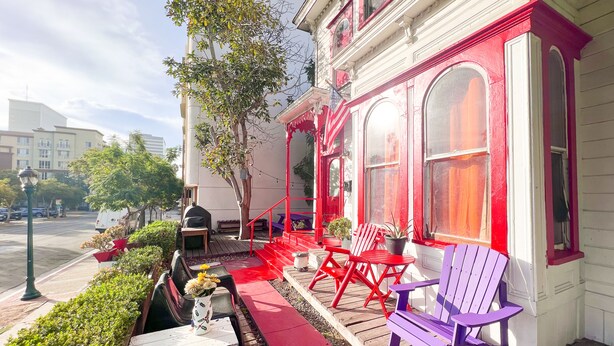 A red and white building with outdoor seating, including red and purple Adirondack chairs, and a small table with a vase of flowers.