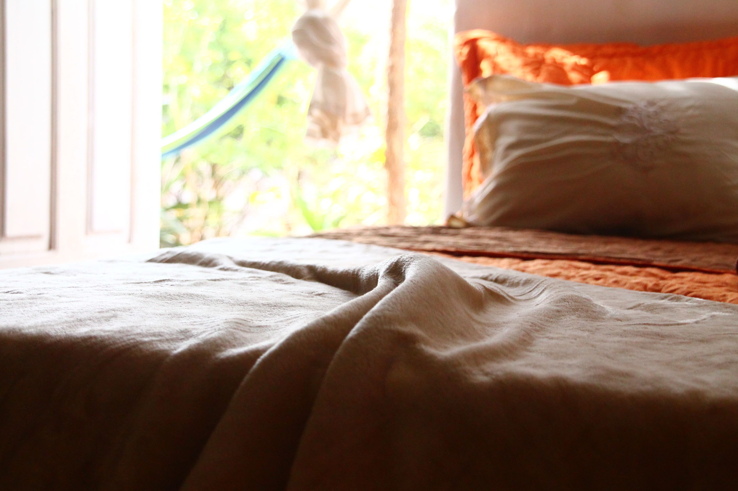 Una cama con una manta blanca y una almohada, una ventana que da a vistas de vegetación.