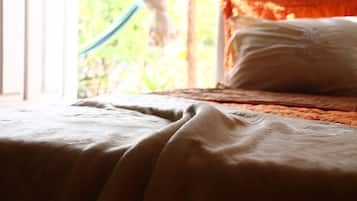 Una cama con una manta blanca y una almohada, una ventana que da a vistas de vegetación.