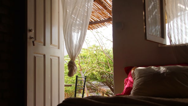 A bedroom with a bed, a chair, and a window with a view of trees. - Farinha de Pau - Eco Rural Project (Tarrafal de Sao Nicolau)