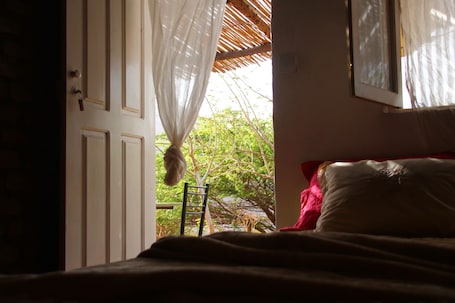 A bedroom with a bed, a chair, and a window with a view of trees.