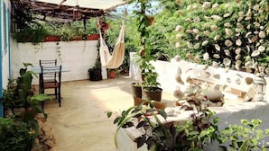A patio with a table and chairs, surrounded by potted plants and hanging hammocks. - Farinha de Pau - Eco Rural Project (Tarrafal de Sao Nicolau)