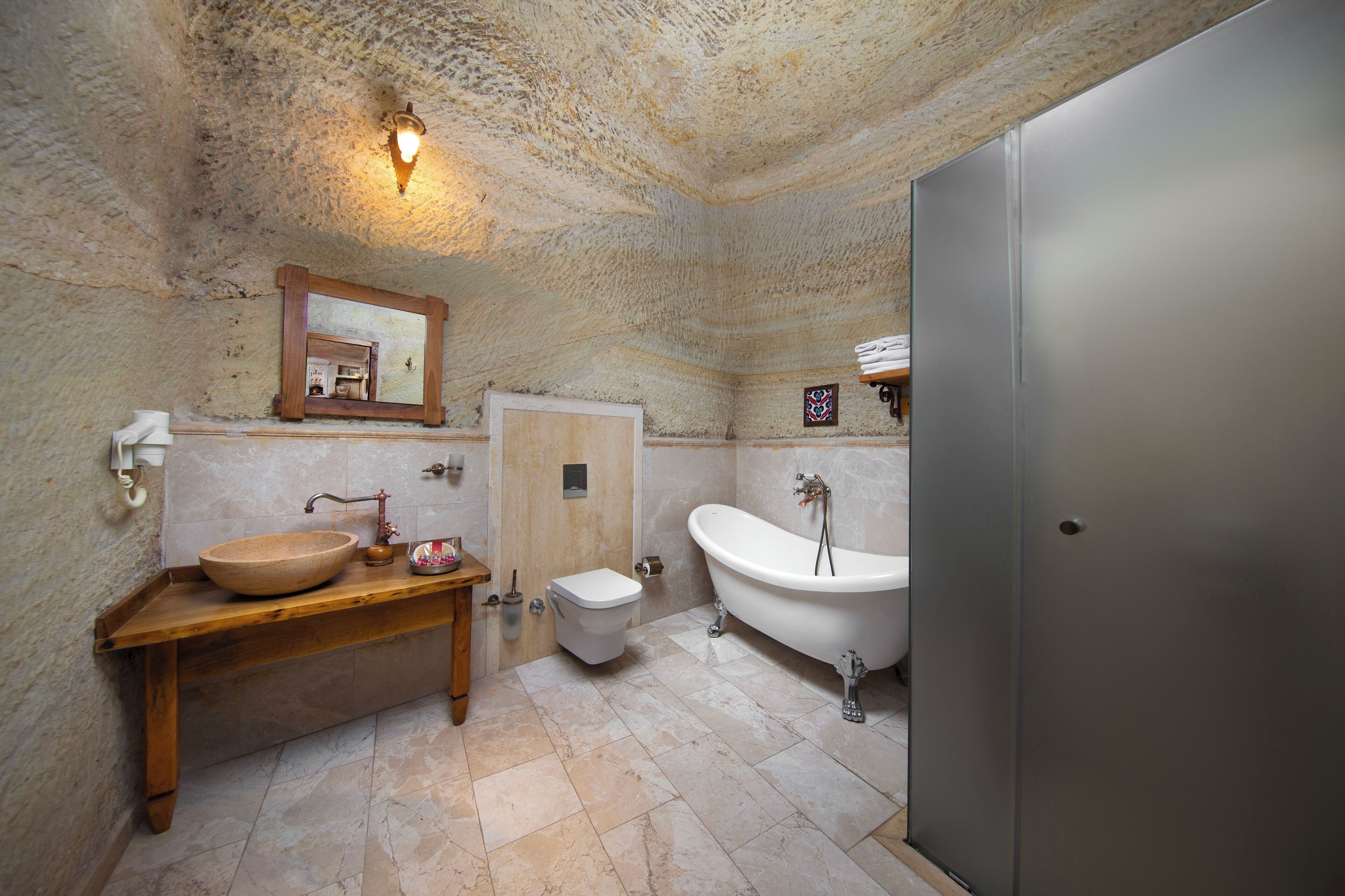 A bathroom with a stone wall, wooden vanity, a freestanding bathtub, and a modern toilet.