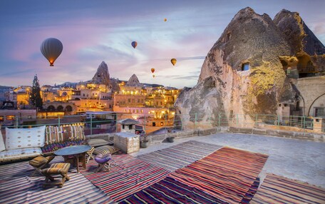 A rooftop terrace with seating and a view of a historic town with unique rock formations and hot air balloons in the sky.