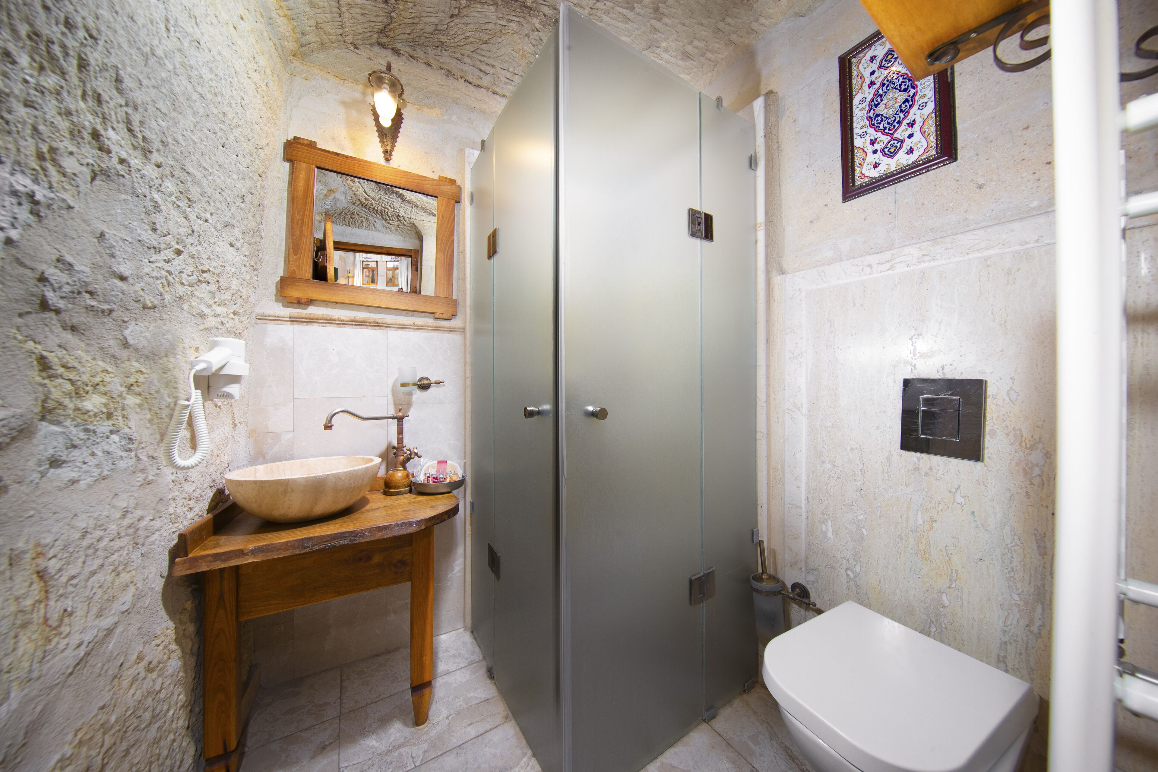 Een badkamer met een houten wastafelmeubel, een wastafel, een spiegel, een deur van geëtst glas en een toilet.