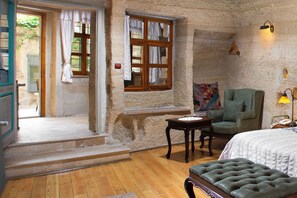 A room with a bed, a green armchair, a small table, and a window with curtains.