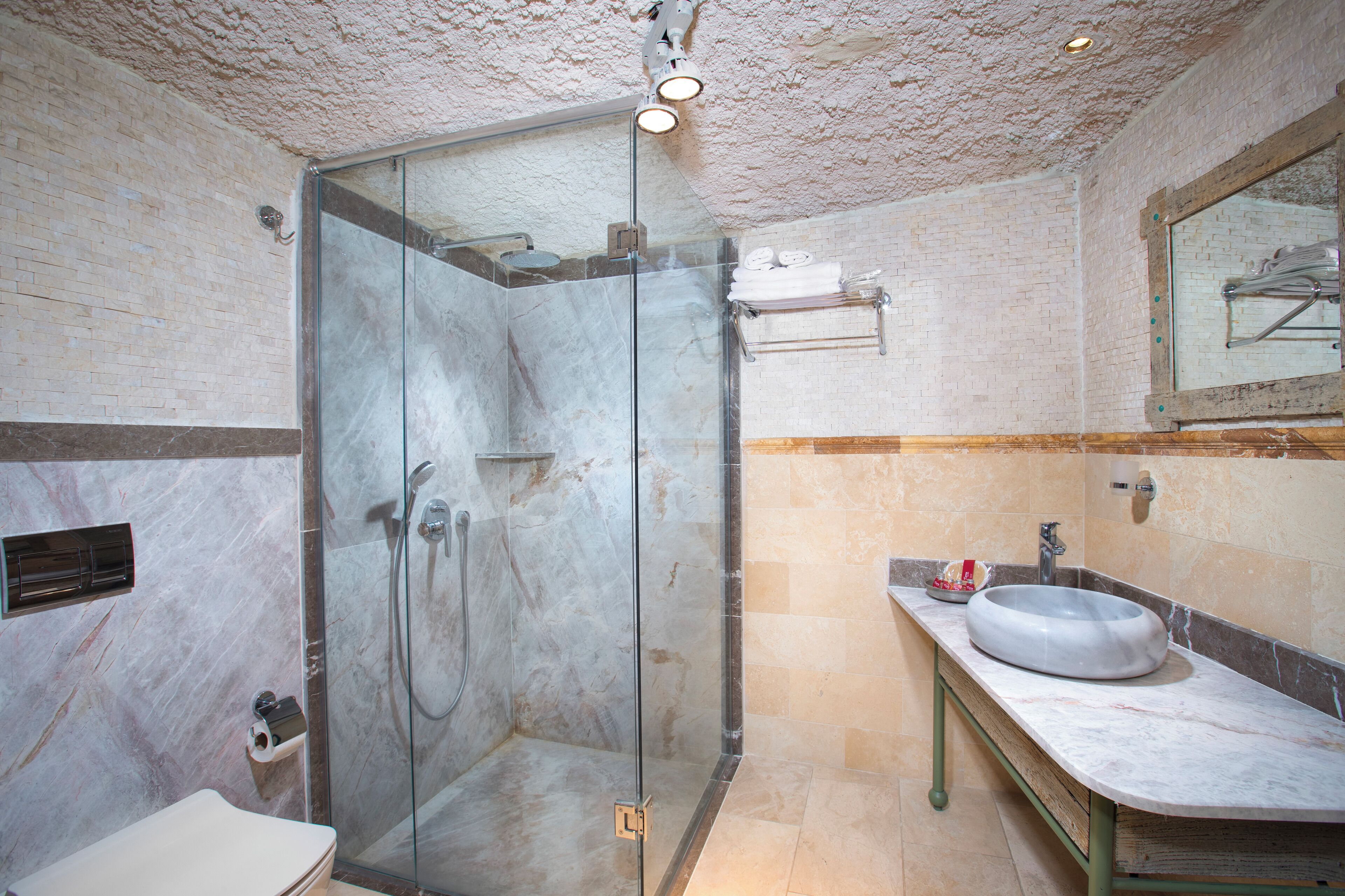 A modern bathroom with a glass-enclosed shower, a marble-tiled shower area, a sink with a marble countertop, and a mirror above the sink.