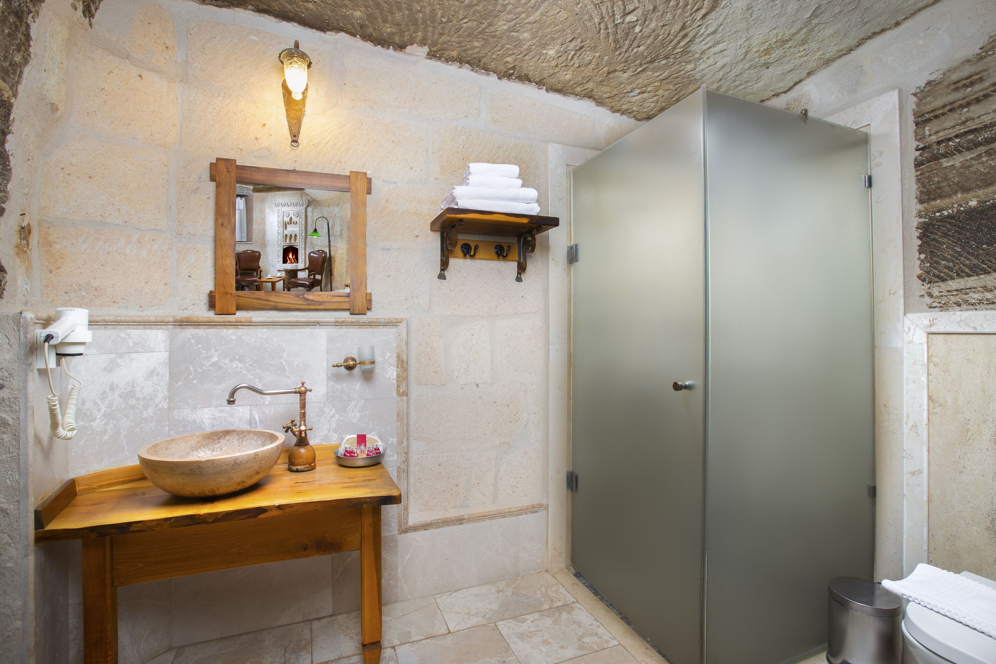 A bathroom with a stone wall, a wooden sink, a mirror, a towel rack, and a cabinet.