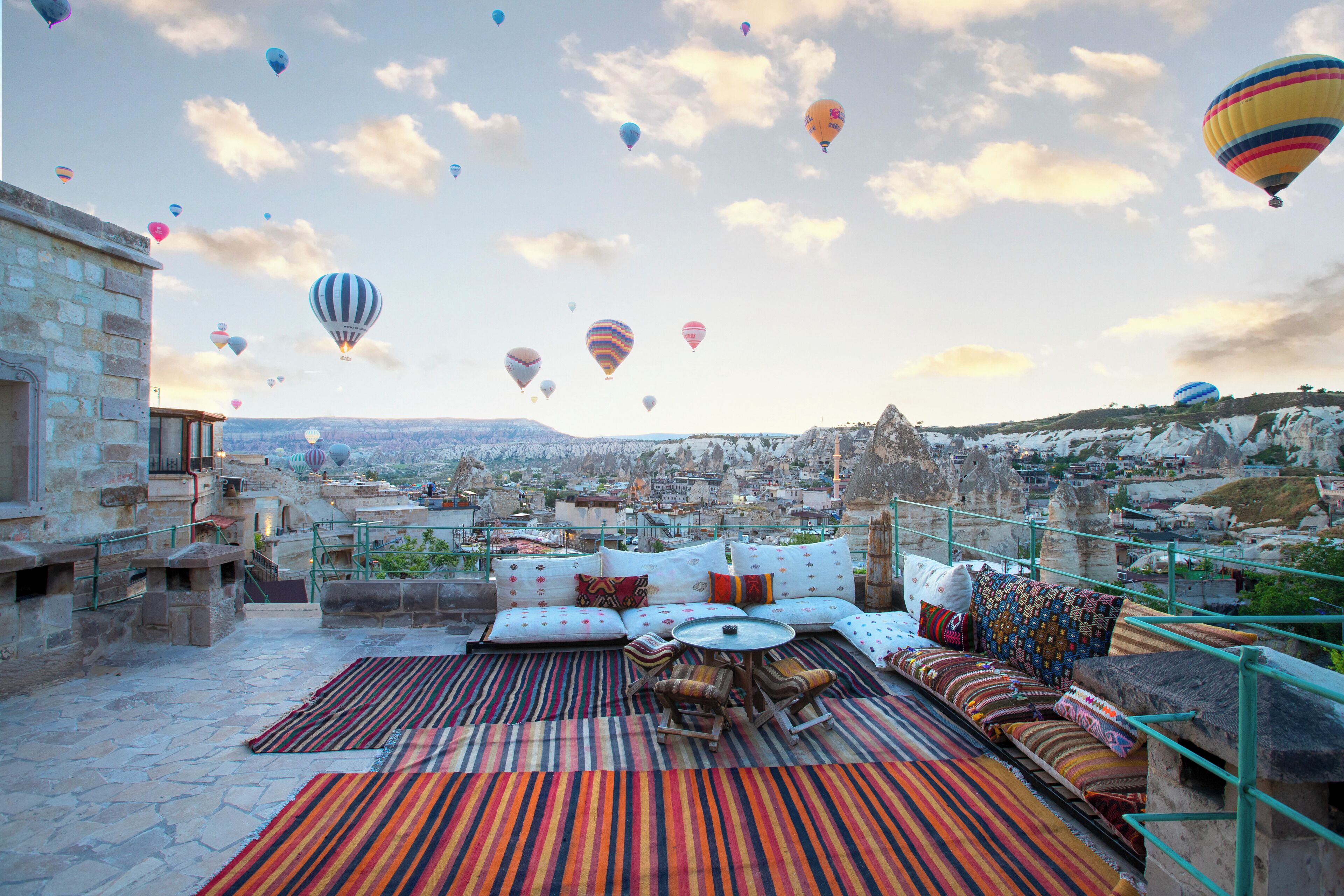 Une terrasse sur le toit, dotée d’un espace salon, de murs en pierre et offrant une vue sur le paysage urbain, avec des montagnes en arrière-plan.
