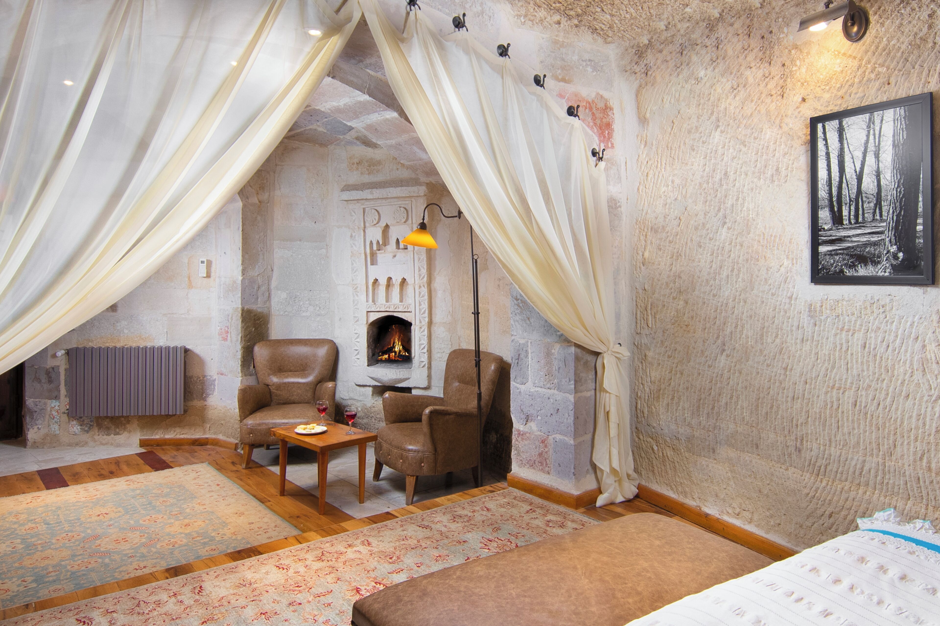 Un cuarto acogedor con chimenea, dos sillones de cuero, una mesita con una copa de vino y una cama.