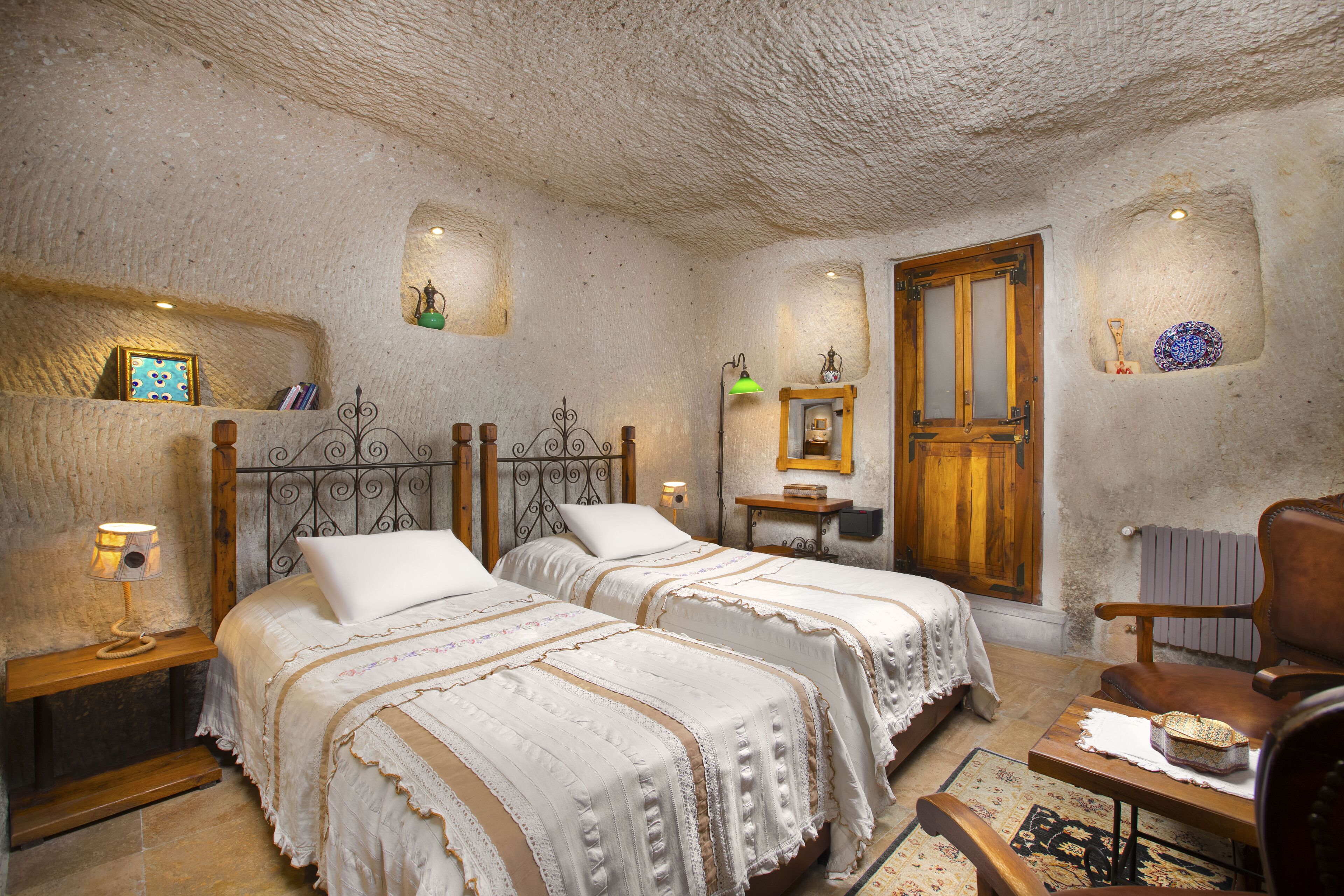 A rustic room with two beds, a wooden chair, a small table, and a radiator.