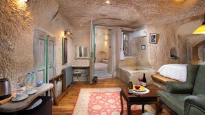 Una habitación rústica con piso de madera, una cama, un sofá, una mesa con una botella y vasos, y un área de cocina con un lavamanos y alacenas.
