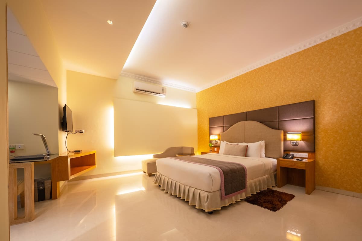 A modern hotel room with a large bed, bedside tables, a desk with a computer, and a TV.