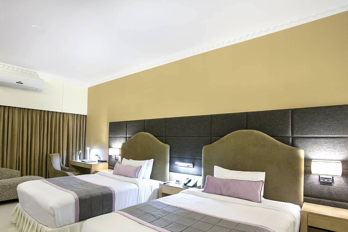 A hotel room with two beds, a sofa, a desk, and an air conditioning unit.