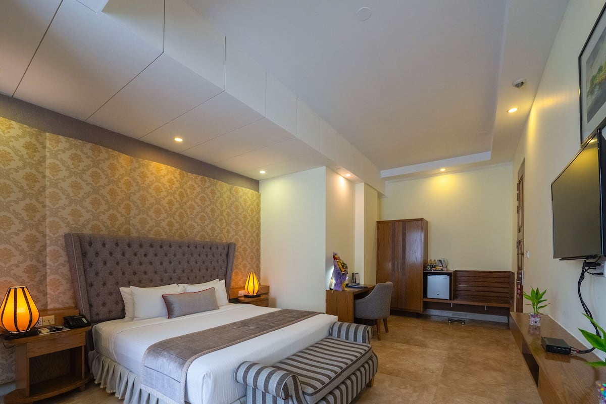 A hotel room with a large bed, bedside lamps, a desk with a computer, a TV, and a small plant.