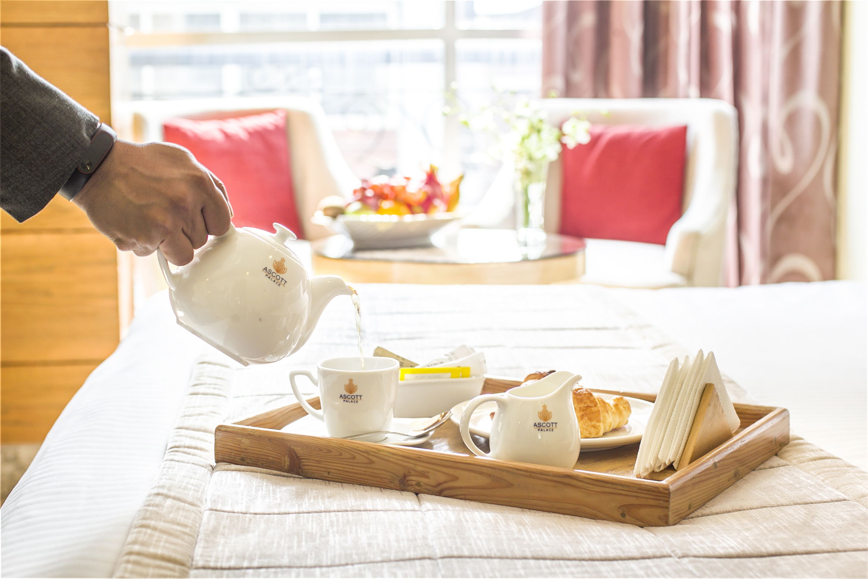 Una bandeja con tetera, dos tazas, una jarra y un croissant sobre una cama.