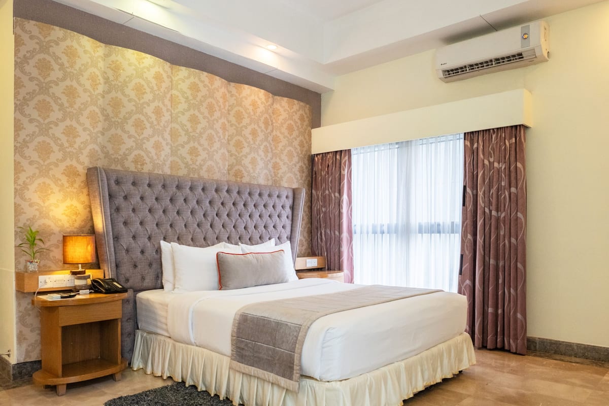 A hotel room with a large bed, a nightstand, a lamp, a telephone, and a window with curtains.
