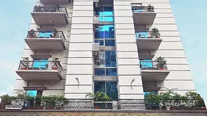 Un edificio de varios pisos con balcones, un letrero que dice 'Ascott Palace Dhaka' y una entrada con puerta de rejas y plantas en macetas.