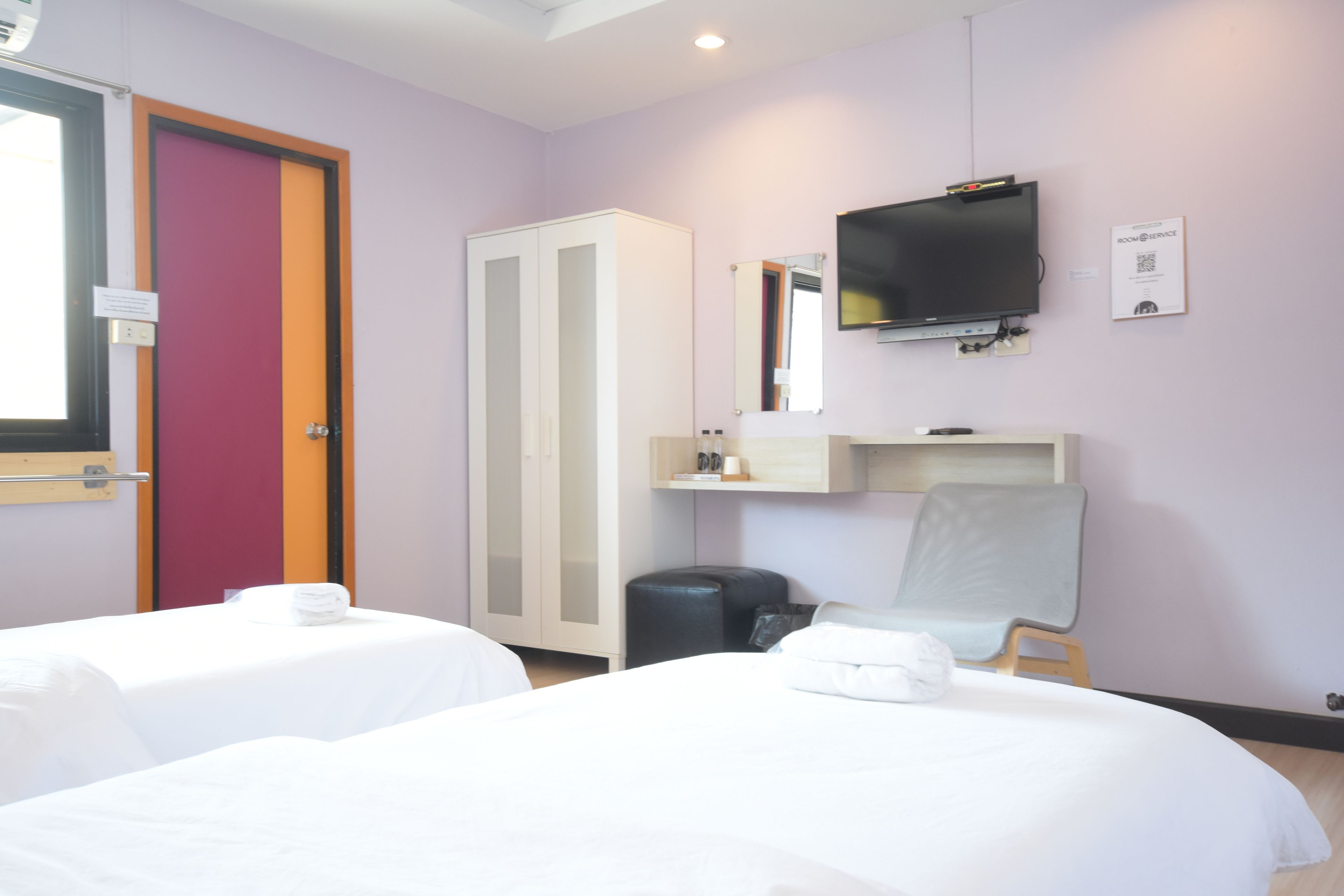 Una camera d'albergo con due letti, una televisione, uno specchio e una scrivania.