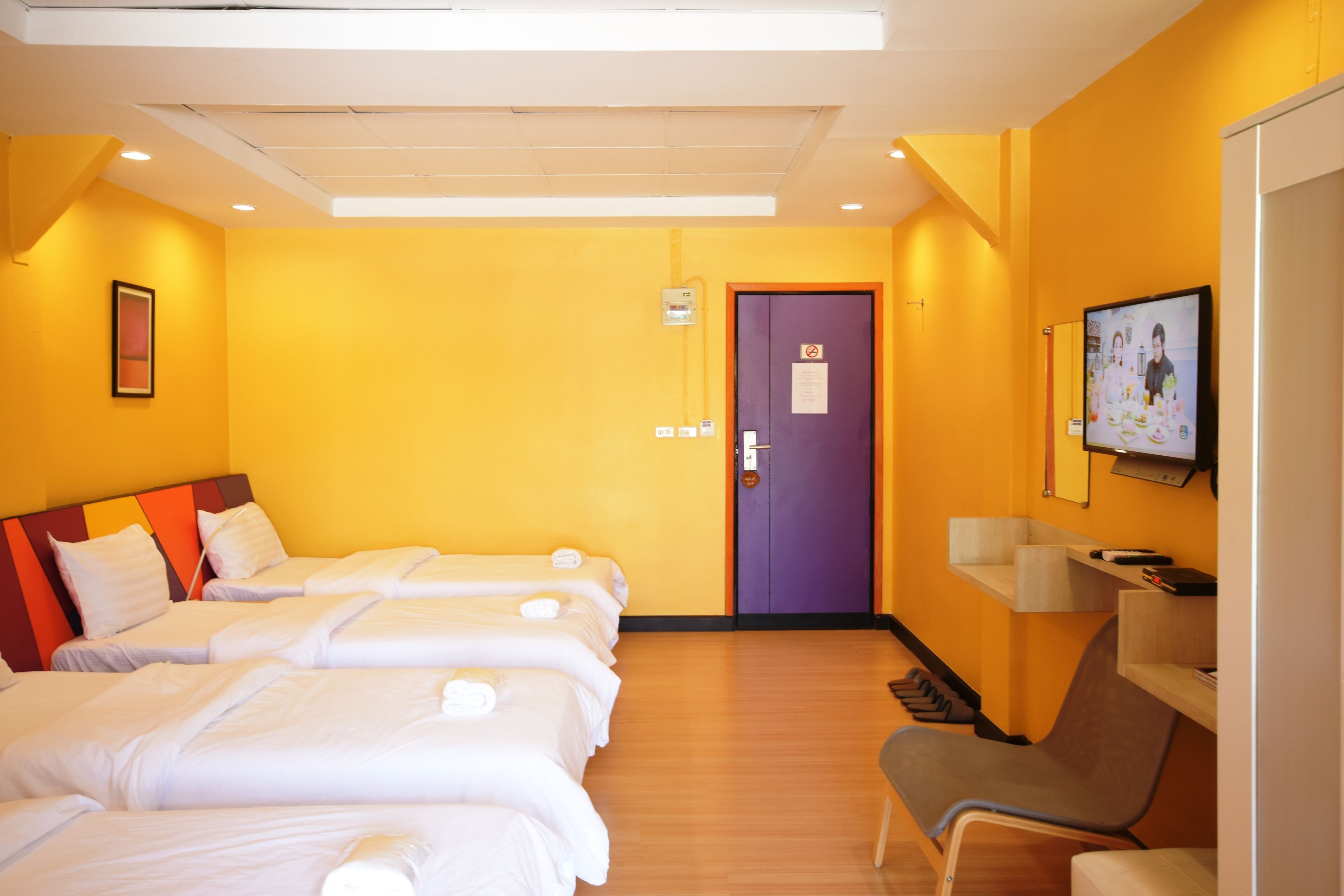A hotel room with three beds, a purple door, and a TV on the wall.