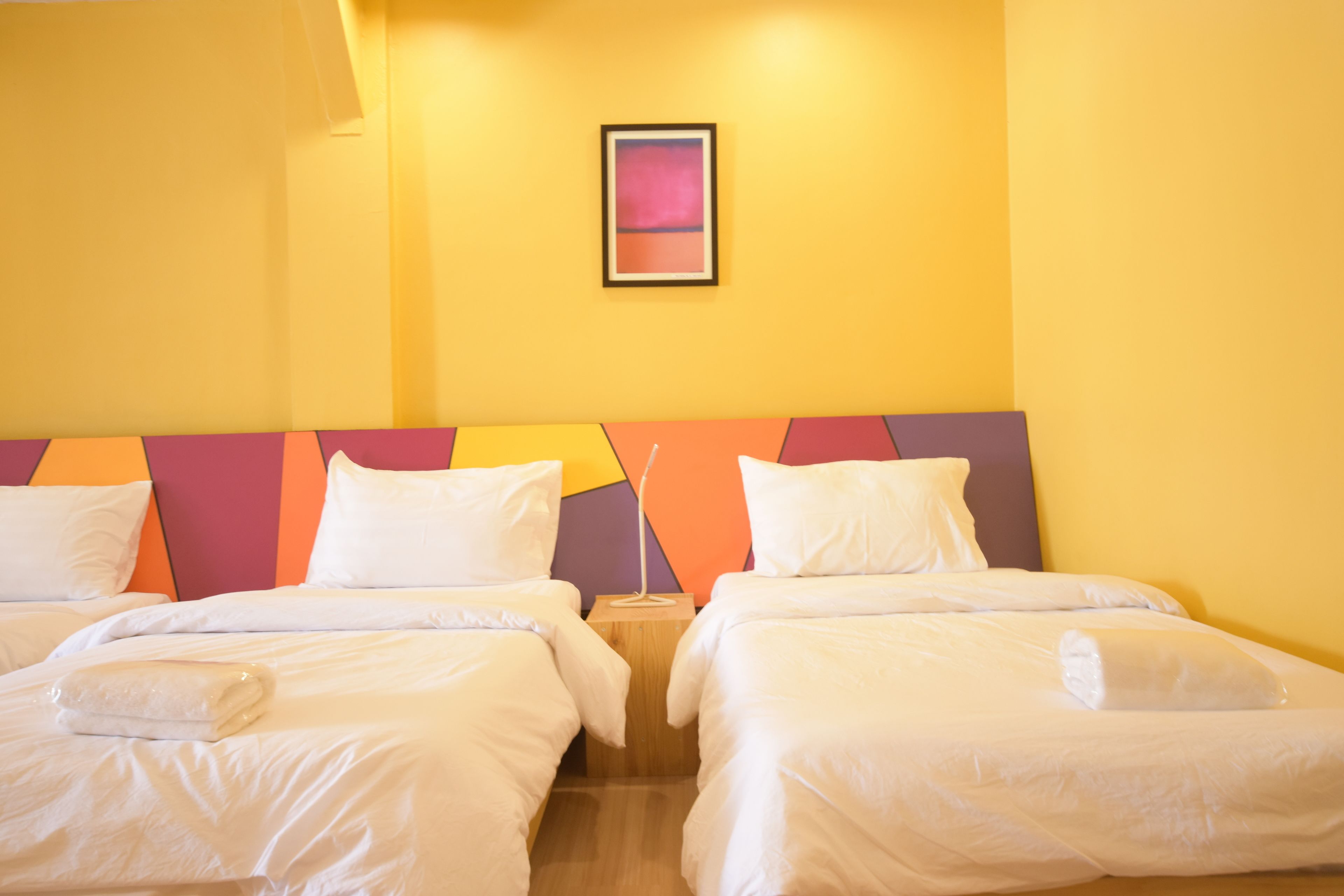 A hotel room with two beds, a nightstand, a lamp, and a framed picture on the wall.