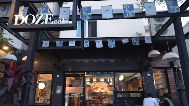 A cafe with a modern design, featuring a prominent DOZE cafe sign, outdoor seating, and a visible interior with tables and chairs. - ROOM at VIPA (Bangkok)