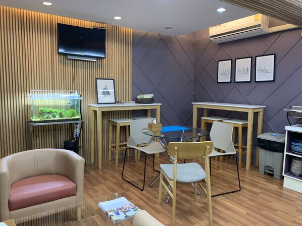 A modern room with a wooden floor, a TV mounted on the wall, a fish tank, and several tables and chairs.