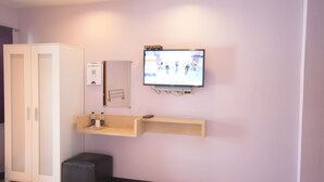 A room with a television mounted on the wall, a wooden shelf, a cabinet, and a small ottoman. - ROOM at VIPA (Bangkok)