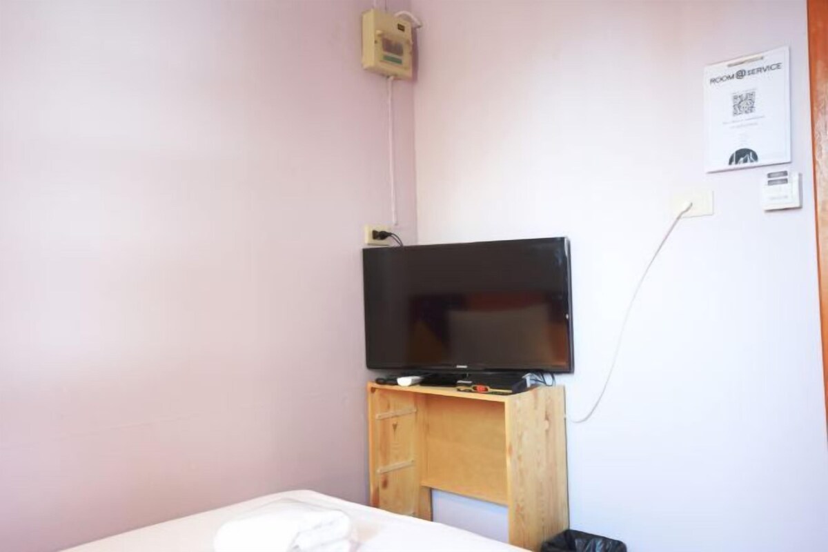 Habitación con cama, un escritorio de madera con televisor, un enchufe en la pared y un código QR para servicio a la habitación.