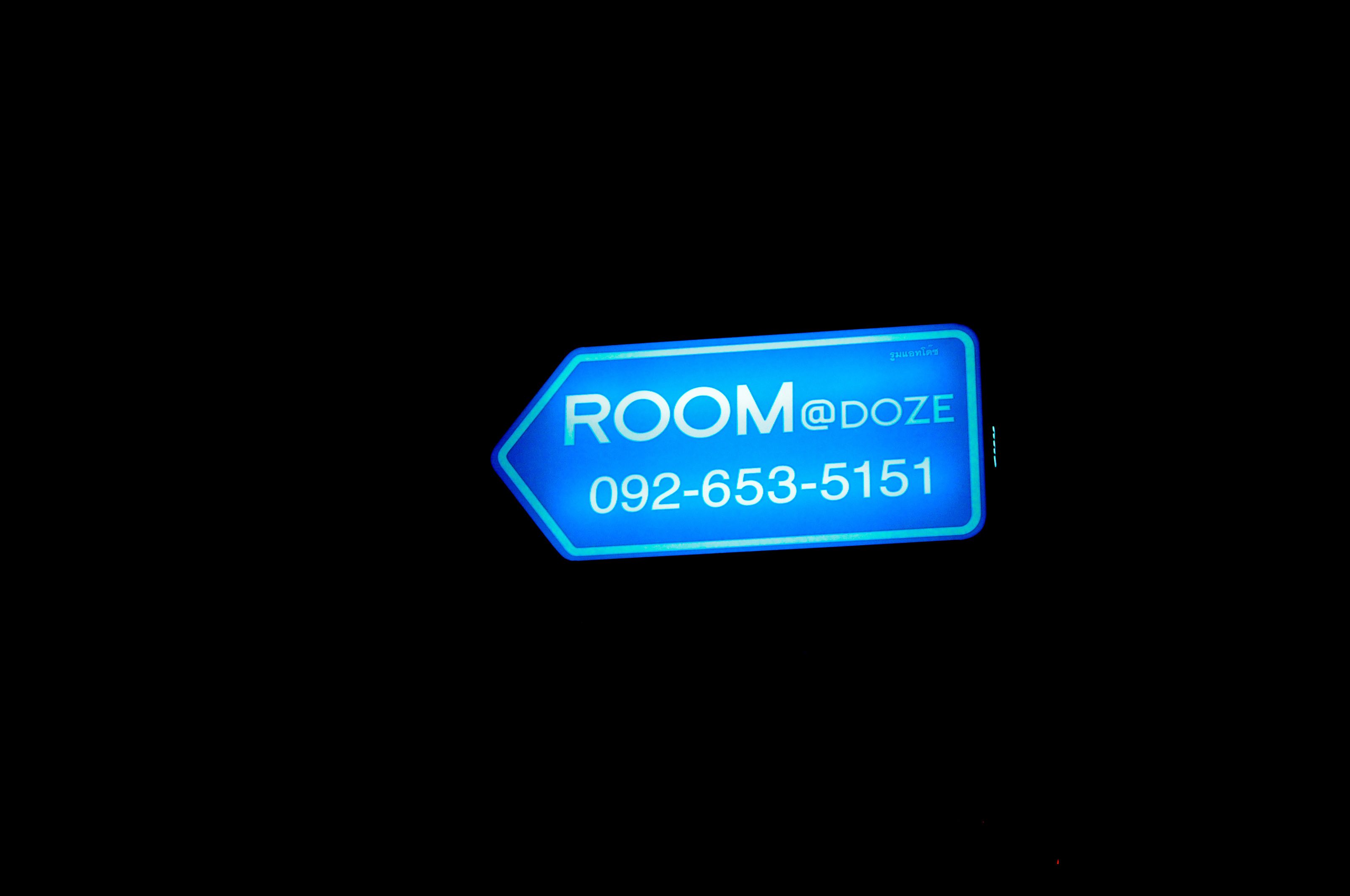 A neon sign with the text "ROOM@DOZE" and a phone number "092-653-5151" against a dark background.