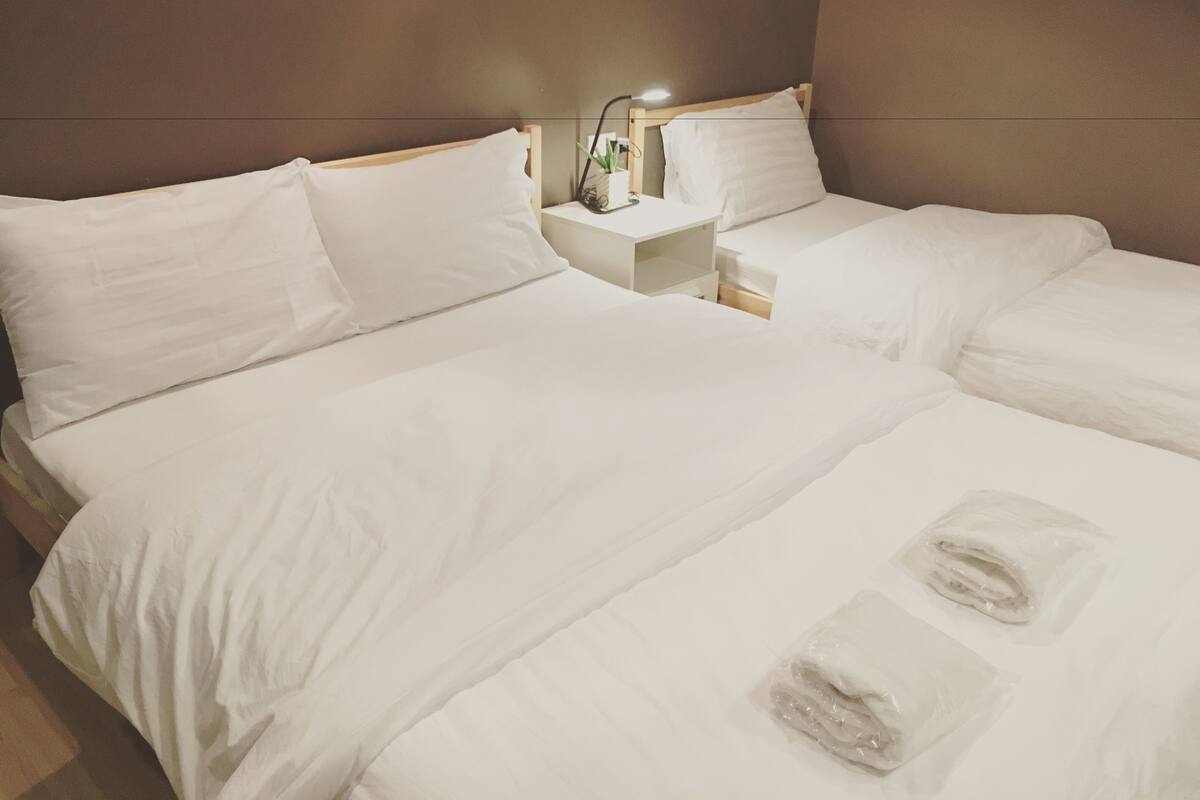 A hotel room with two beds, white linens, a nightstand with a lamp, and a small potted plant.