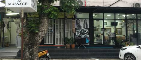 Un centro de spa y masajes con un letrero, un árbol, una motocicleta estacionada y un coche blanco al frente.