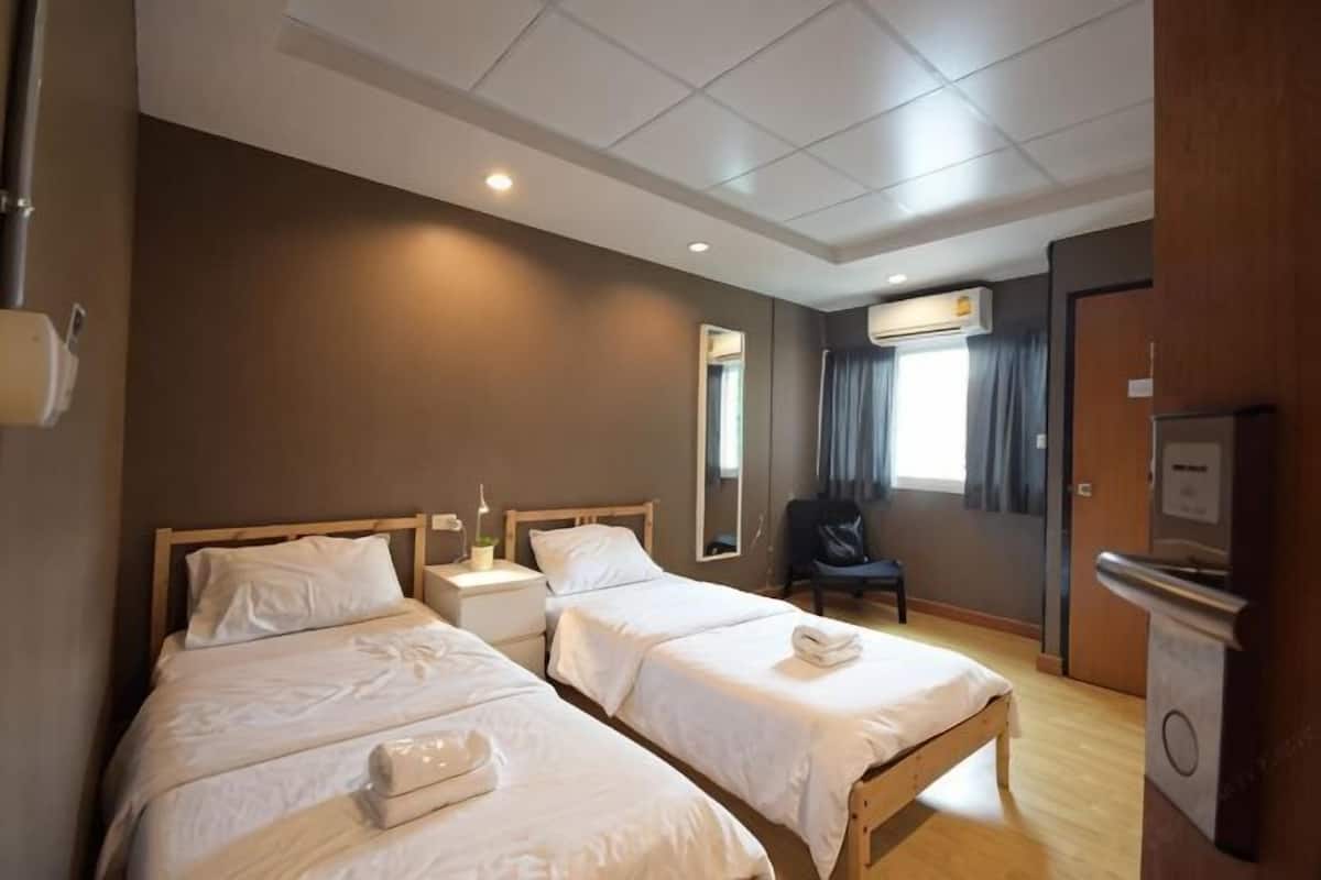 A hotel room with two beds, a desk, a chair, a TV, and a window with curtains.