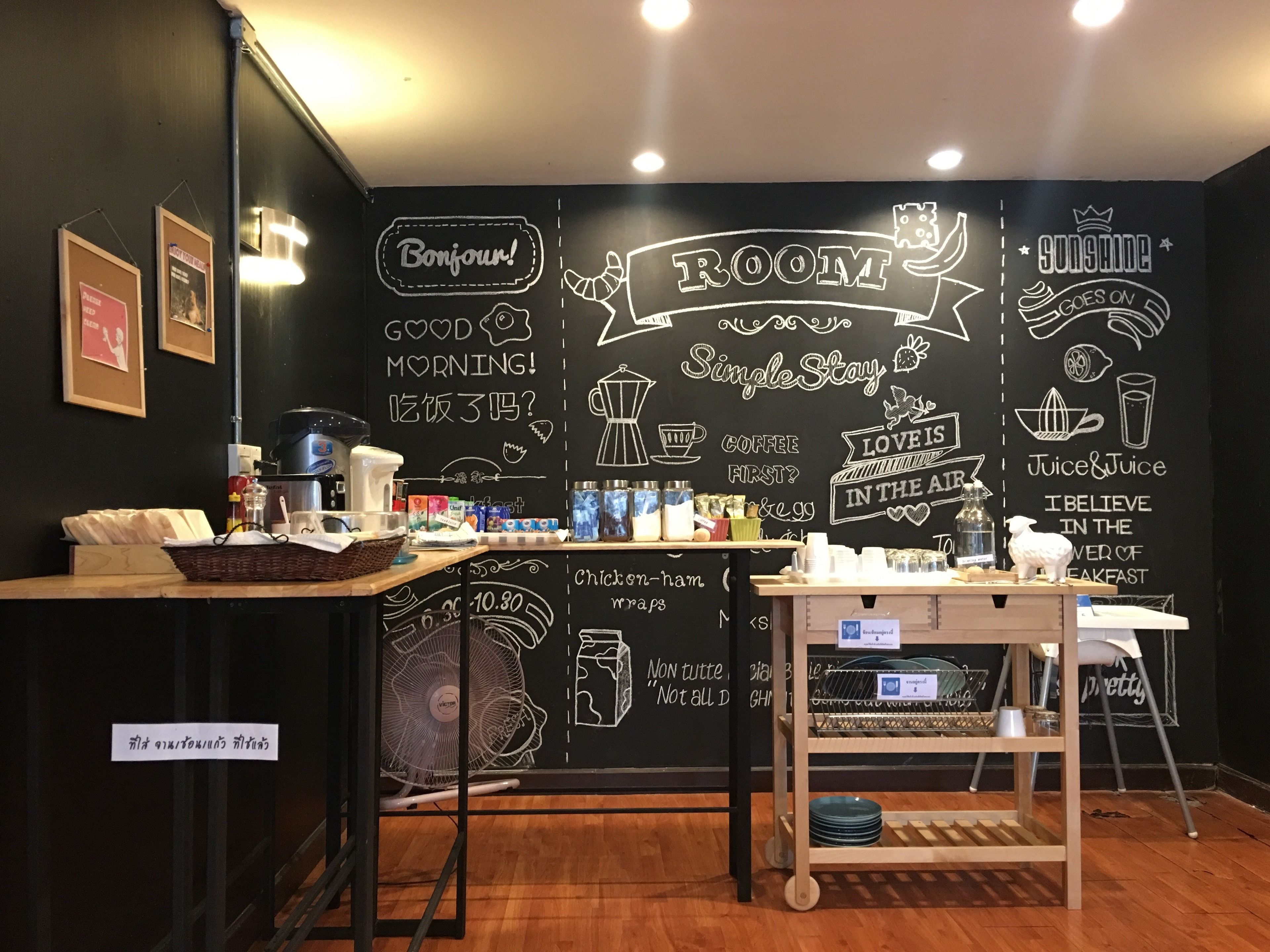 Een café met een prikbord waarop verschillende zinnen en tekeningen staan, een koffieapparaat en een ventilator.