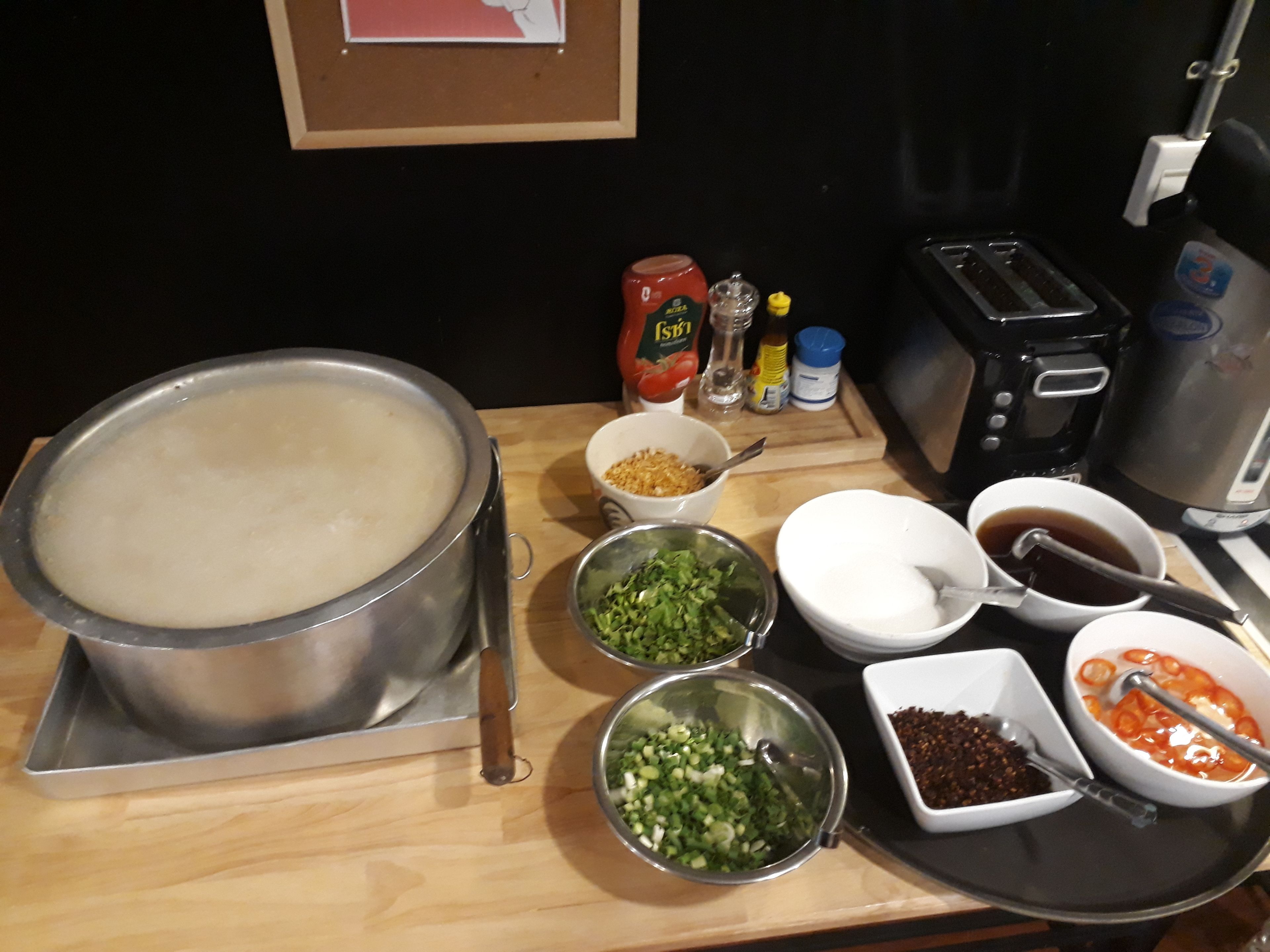 En køkkenbordplade med en stor gryde suppe, forskellige skåle med ingredienser, samt en kaffemaskine.