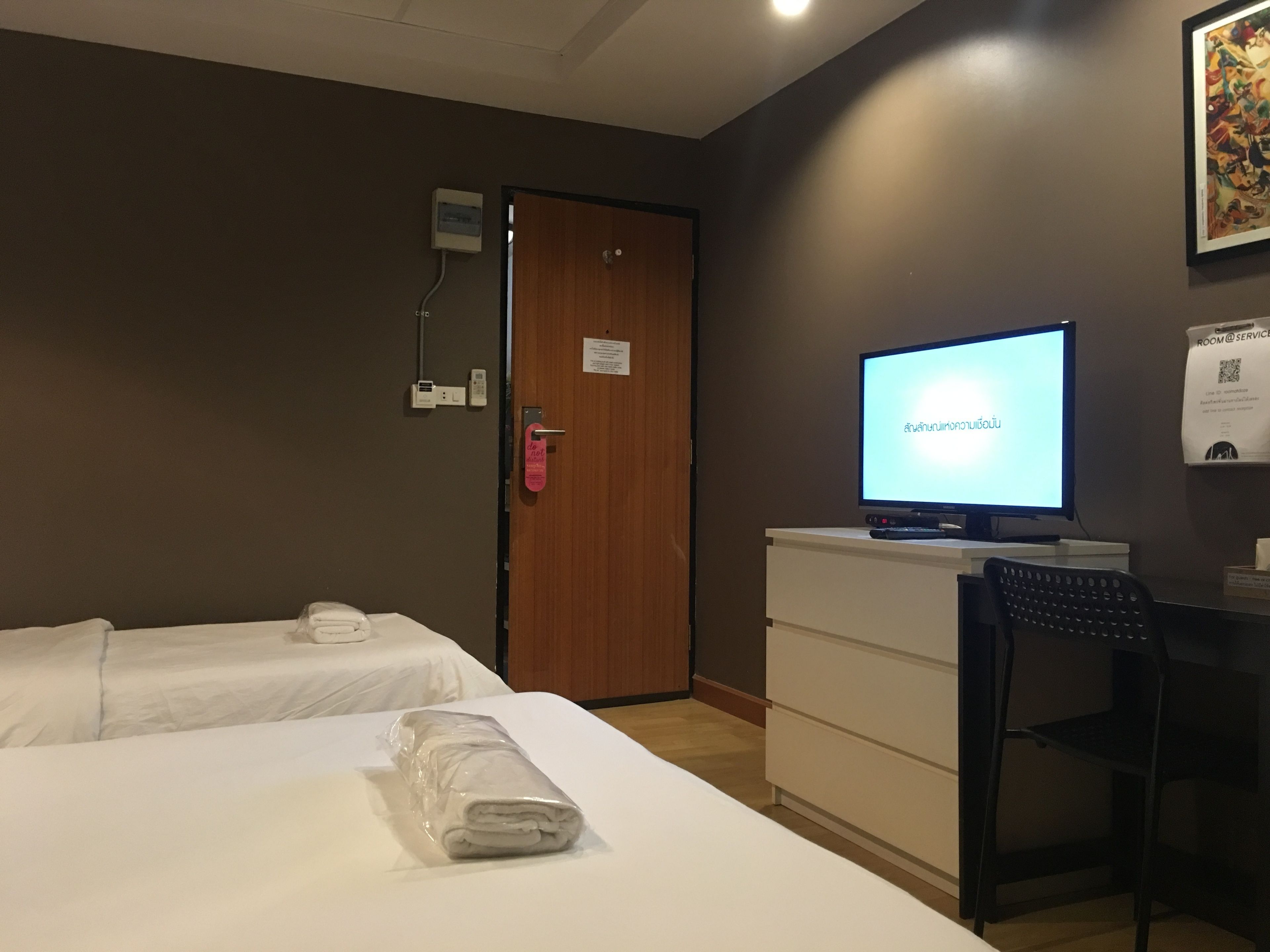 A hotel room with two beds, a desk with a computer, a chair, and a door with a 'Do Not Disturb' sign.