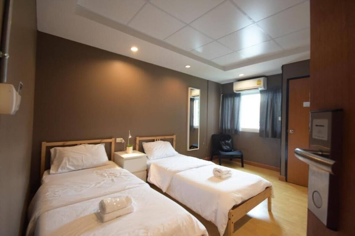 A hotel room with two beds, a desk, a chair, a mirror, and an air conditioning unit.