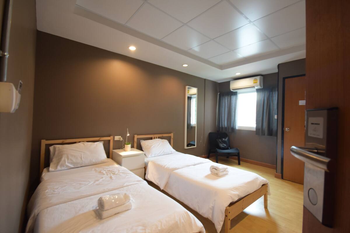 A hotel room with two beds, a desk, a chair, and a minibar.