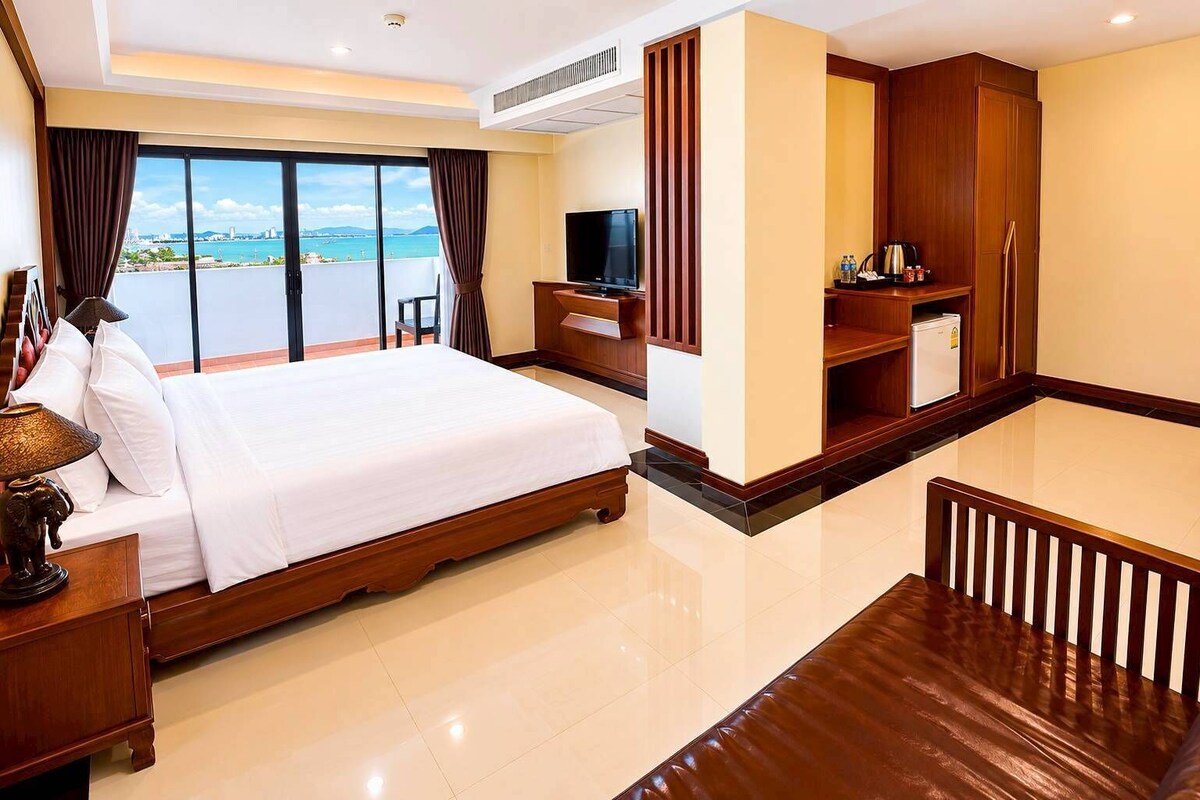Een hotelkamer met een groot bed, een televisie, een bureau en uitzicht op zee.