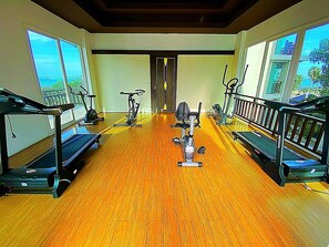 Een sportschool met trainingsapparatuur, grote ramen en een houten vloer.