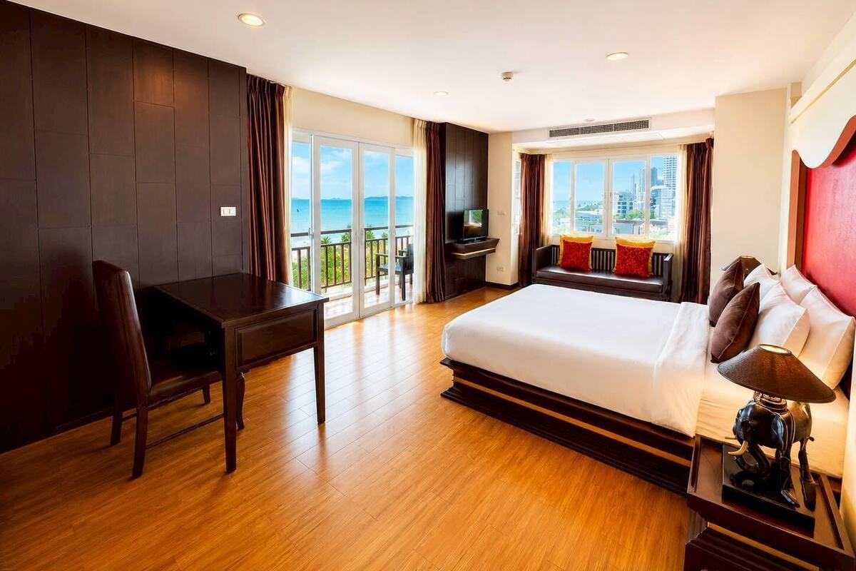 Een hotelkamer met een groot bed, een bureau, een stoel, een televisie en een balkon met uitzicht op de stad.