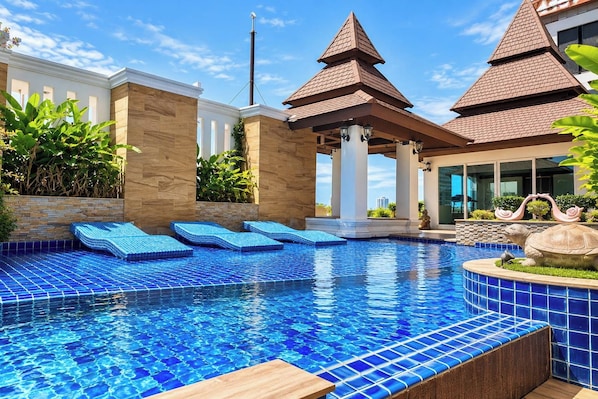 A swimming pool with blue tiles, lounge chairs, and a decorative turtle statue.