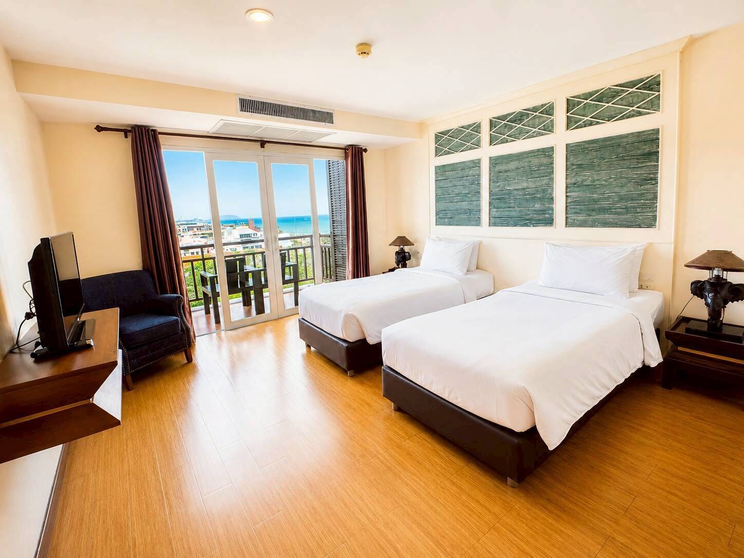 A hotel room with two beds, a TV, a desk, and a balcony with a view.