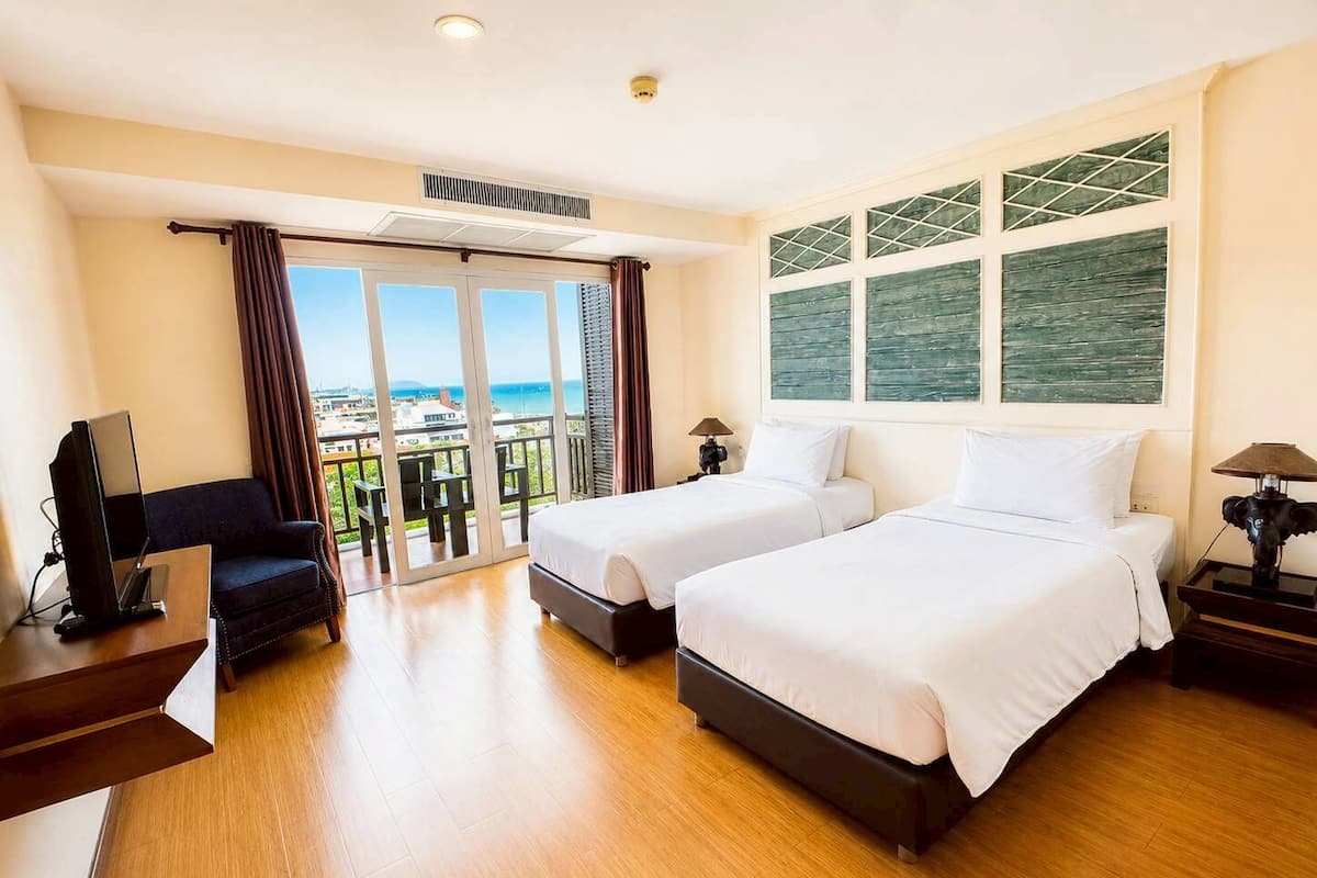 A hotel room with two beds, a TV, a desk, and a balcony with a view.