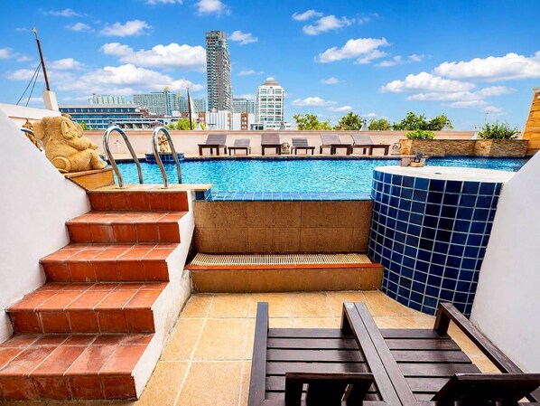 Piscina en la azotea con escalones que bajan a un área de descanso, rodeada de edificios de la ciudad.
