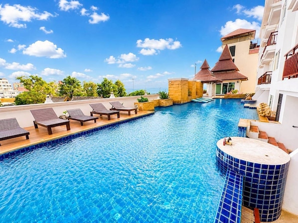 A swimming pool with lounge chairs, a stone structure, and a building with a tiled roof. - Royal Heritage Pavillion (Pattaya)