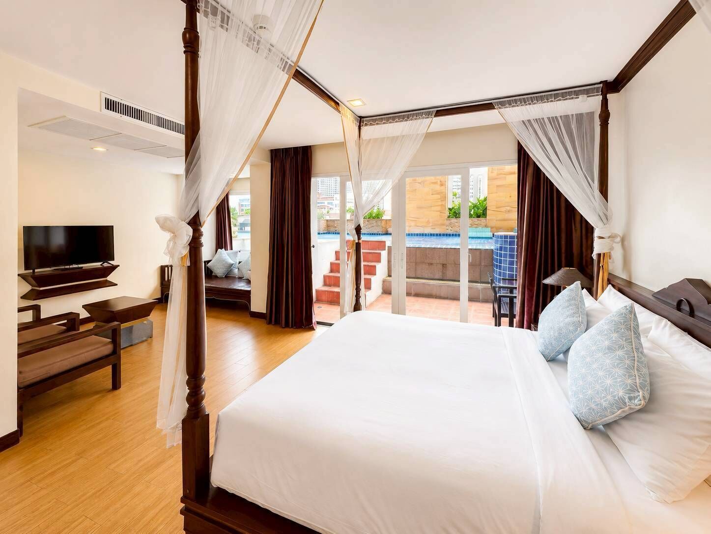 Ein Schlafzimmer mit Himmelbett, Fernseher und Balkon mit Blick auf einen Pool.