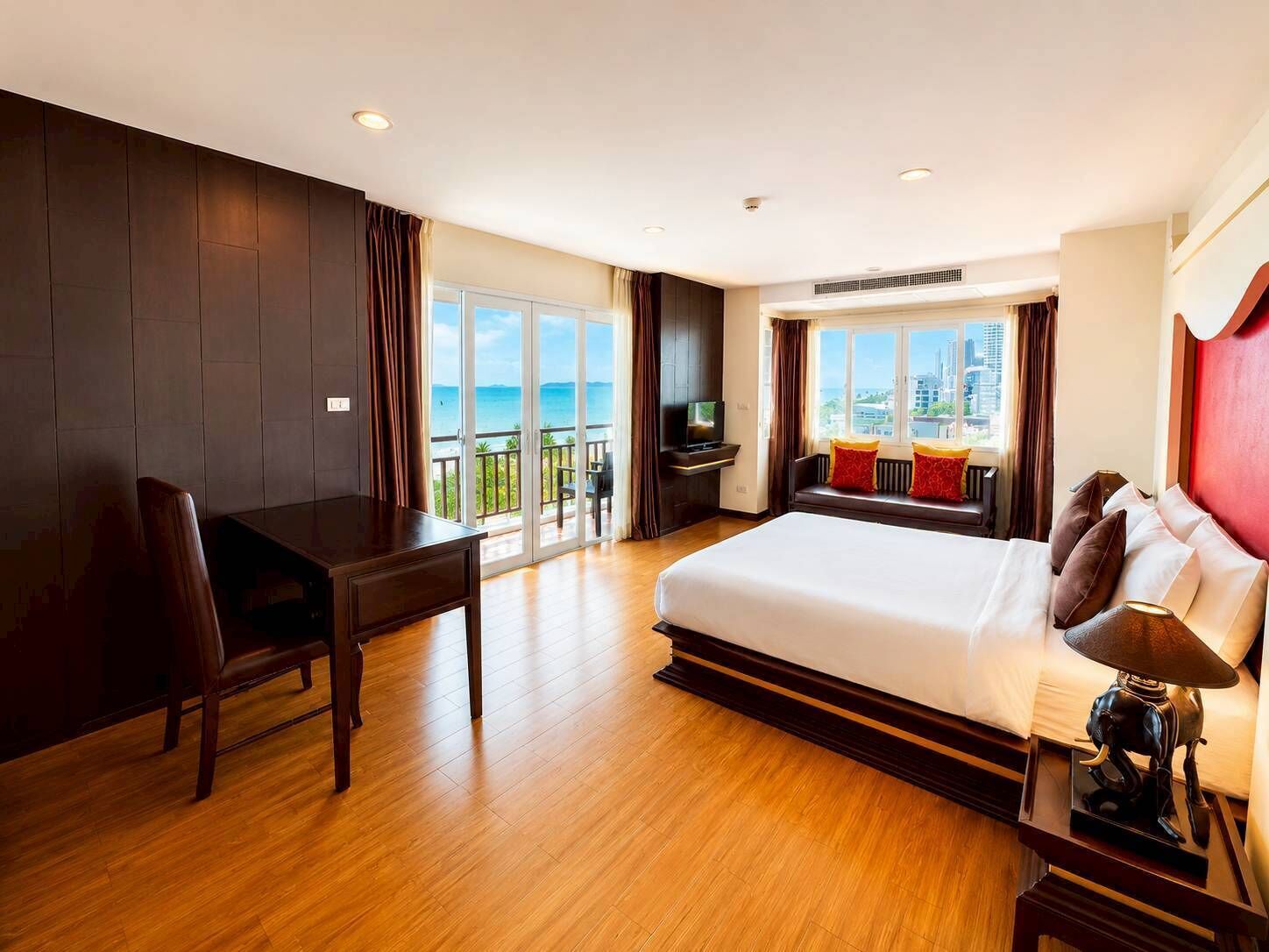 Ein Hotelzimmer mit einem großen Bett, einem Schreibtisch, einem Sessel, einem Fernseher und einem Balkon mit Blick auf die Stadt.